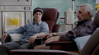 Movie still from “50/50” (2011), directed by Jonathan Levine – A man sitting next to another man in a hospital room; Medium shot, Over the shoulder angle