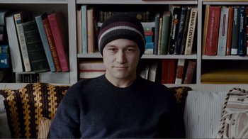 Movie still from “50/50” (2011), directed by Jonathan Levine – A man wearing a hat sitting in front of a book shelf; Close Up shot, Over the shoulder angle