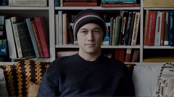 Movie still from “50/50” (2011), directed by Jonathan Levine – A man sitting in front of a book shelf wearing a hat; Close Up shot, High angle