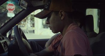 Movie still from “600 Miles” (2015), directed by Gabriel Ripstein – A young man in a baseball cap is driving a car; Close Up shot, Low angle