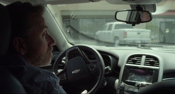 Movie still from “600 Miles” (2015), directed by Gabriel Ripstein – A man sitting in the driver's seat of a car driving down a street; Close Up shot, Over the shoulder angle
