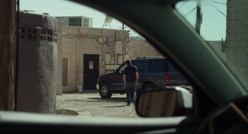 Movie still from “600 Miles” (2015), directed by Gabriel Ripstein – A man standing in front of a parked car; Wide shot, Over the shoulder angle