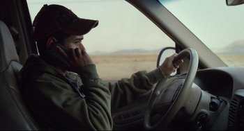 Movie still from “600 Miles” (2015), directed by Gabriel Ripstein – A man sitting in the drivers seat of a car while talking on a cell phone; Medium shot, Over the shoulder angle
