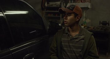 Movie still from “600 Miles” (2015), directed by Gabriel Ripstein – A young man wearing a hat sitting next to a car; Medium shot, Over the shoulder angle