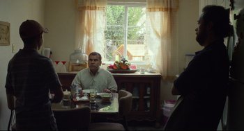 Movie still from “600 Miles” (2015), directed by Gabriel Ripstein – A man sitting at a table with a plate in front of him; Medium shot, Over the shoulder angle