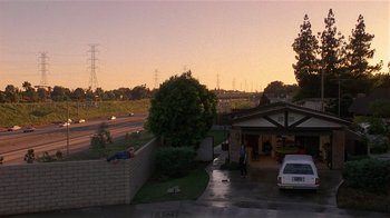 Movie still from “8 Million Ways to Die” (1986), directed by Hal Ashby – A man laying on the side of the road next to a house; Extreme Wide shot, Low angle