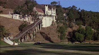 Movie still from “8 Million Ways to Die” (1986), directed by Hal Ashby – A car parked in front of a building on a hill; Extreme Wide shot, High angle