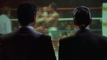 Movie still from “8 Million Ways to Die” (1986), directed by Hal Ashby – Two men in suits looking at a screen; Medium shot, Over the shoulder angle