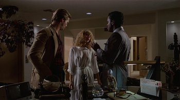 Movie still from “8 Million Ways to Die” (1986), directed by Hal Ashby – A man and two women standing next to each other in a room; Medium shot, Over the shoulder angle