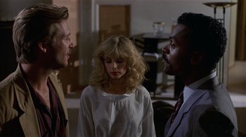 Movie still from “8 Million Ways to Die” (1986), directed by Hal Ashby – Two men and a woman talking to each other in a room; Medium shot, Over the shoulder angle
