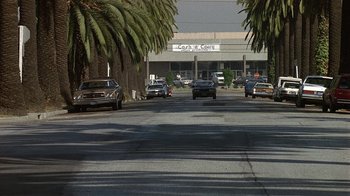 Movie still from “8 Million Ways to Die” (1986), directed by Hal Ashby – Cars driving down a street lined with palm trees; Extreme Wide shot, Low angle