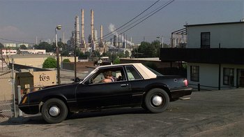 Movie still from “8 Million Ways to Die” (1986), directed by Hal Ashby – A man driving a car in front of an oil refinery; Extreme Wide shot, Low angle