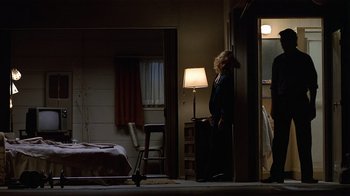 Movie still from “8 Million Ways to Die” (1986), directed by Hal Ashby – A woman standing in a dark room next to a bed; Wide shot, Low angle