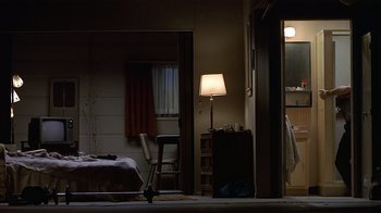 Movie still from “8 Million Ways to Die” (1986), directed by Hal Ashby – A room with a bed , a chair , a lamp , and a window; Wide shot, Low angle