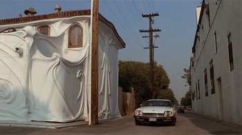 Movie still from “8 Million Ways to Die” (1986), directed by Hal Ashby – A car parked on the side of the road next to a building; Extreme Wide shot, Low angle