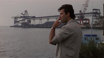 Movie still from “8 Million Ways to Die” (1986), directed by Hal Ashby – A man standing next to a body of water; Medium shot, Over the shoulder angle