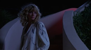 Movie still from “8 Million Ways to Die” (1986), directed by Hal Ashby – A woman with blonde hair standing next to a building at night; Medium shot, Low angle