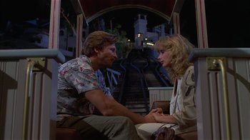 Movie still from “8 Million Ways to Die” (1986), directed by Hal Ashby – A man and a woman sitting next to each other on a train platform; Medium shot, Over the shoulder angle