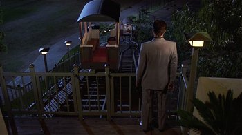 Movie still from “8 Million Ways to Die” (1986), directed by Hal Ashby – A man in a suit standing next to a train; Wide shot, High angle
