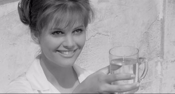 Movie still from “8½” (1963), directed by Federico Fellini – A woman is holding a glass of water and smiling for the camera; Close Up shot, Over the shoulder angle