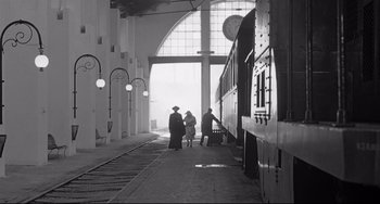 Movie still from “8½” (1963), directed by Federico Fellini – Two people are standing in a train station next to a train car; Extreme Wide shot, Low angle