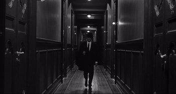 Movie still from “8½” (1963), directed by Federico Fellini – A black and white photo of a man walking down a hall way; Wide shot, High angle