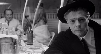 Movie still from “8½” (1963), directed by Federico Fellini – An older woman sitting at an outdoor table with wine; Close Up shot, Over the shoulder angle