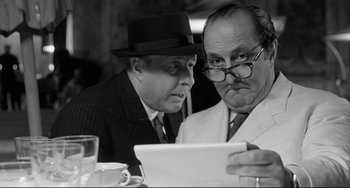 Movie still from “8½” (1963), directed by Federico Fellini – Two men are looking at a tablet in a restaurant; Close Up shot, Over the shoulder angle