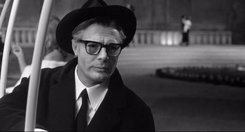 Movie still from “8½” (1963), directed by Federico Fellini – A black and white photo of a man wearing a hat and glasses; Close Up shot, Over the shoulder angle