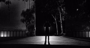 Movie still from “8½” (1963), directed by Federico Fellini – A man standing in the dark in front of some trees; Wide shot, Low angle