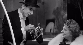 Movie still from “8½” (1963), directed by Federico Fellini – A man in a top hat holding a camera and looking at a woman; Close Up shot, Over the shoulder angle