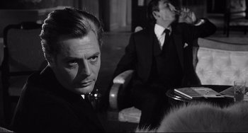 Movie still from “8½” (1963), directed by Federico Fellini – A man in a suit sitting next to another man in a suit; Close Up shot, Over the shoulder angle