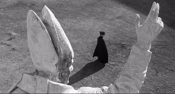 Movie still from “8½” (1963), directed by Federico Fellini – A man in a black cape walking on a dirt path; Extreme Wide shot, High angle