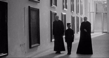 Movie still from “8½” (1963), directed by Federico Fellini – A man and a boy are standing in front of a building; Wide shot, Low angle