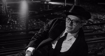 Movie still from “8½” (1963), directed by Federico Fellini – A man wearing a hat and glasses sitting on a chair; Close Up shot, Low angle
