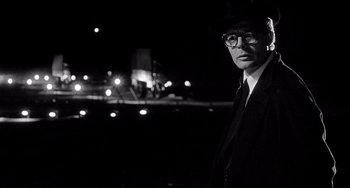 Movie still from “8½” (1963), directed by Federico Fellini – A man in a suit and hat standing in the dark; Medium shot, Low angle