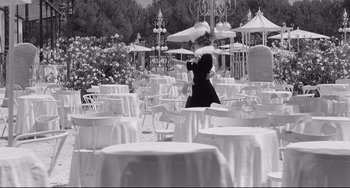 Movie still from “8½” (1963), directed by Federico Fellini – A woman in a long black dress standing in front of tables with white umbrellas; Wide shot, High angle