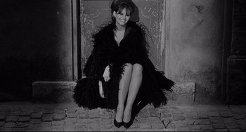 Movie still from “8½” (1963), directed by Federico Fellini – A woman sitting on the ground wearing a black dress; Medium shot, High angle