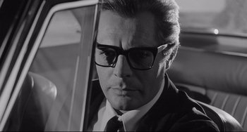 Movie still from “8½” (1963), directed by Federico Fellini – Black and white photograph of a man in a suit and glasses; Close Up shot, Low angle