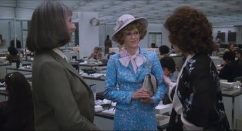 Movie still from “9 to 5” (1980), directed by Colin Higgins – A woman in a blue dress talking to two other women in an office setting; Medium shot, Over the shoulder angle