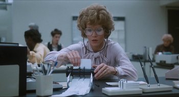 Movie still from “9 to 5” (1980), directed by Colin Higgins – An older woman in glasses typing on a typewriter in an office setting; Medium shot, Low angle