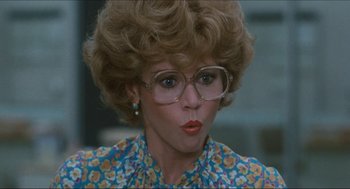 Movie still from “9 to 5” (1980), directed by Colin Higgins – A person wearing glasses and a wig; Close Up shot, Over the shoulder angle