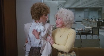Movie still from “9 to 5” (1980), directed by Colin Higgins – Two women are standing next to each other and talking; Medium shot, Over the shoulder angle