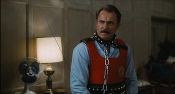 Movie still from “9 to 5” (1980), directed by Colin Higgins – A man in a red vest and a chain around his neck; Medium shot, Low angle