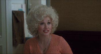 Movie still from “9 to 5” (1980), directed by Colin Higgins – A woman with a blonde wig sitting in front of a window; Medium shot, Over the shoulder angle