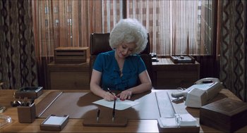 Movie still from “9 to 5” (1980), directed by Colin Higgins – A woman sitting at a desk writing on a piece of paper; Medium shot, High angle
