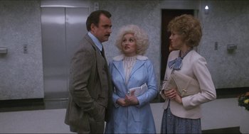 Movie still from “9 to 5” (1980), directed by Colin Higgins – A man and two women standing next to each other in front of an elevator; Medium shot, Over the shoulder angle
