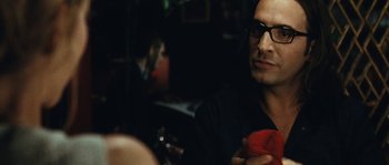 Movie still from “99 Francs” (2007), directed by Jan Kounen – A man sitting at a table holding a red object; Close Up shot, Over the shoulder angle