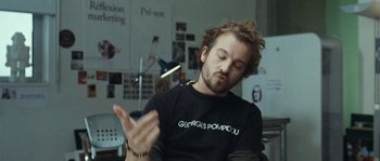 Movie still from “99 Francs” (2007), directed by Jan Kounen – A man with a beard and mustache is holding something in his hand; Close Up shot, Low angle