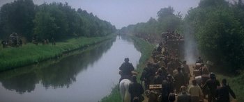 Movie still from “A Bridge Too Far” (1977), directed by Richard Attenborough – A group of people on a horse next to a body of water; Extreme Wide shot, High angle